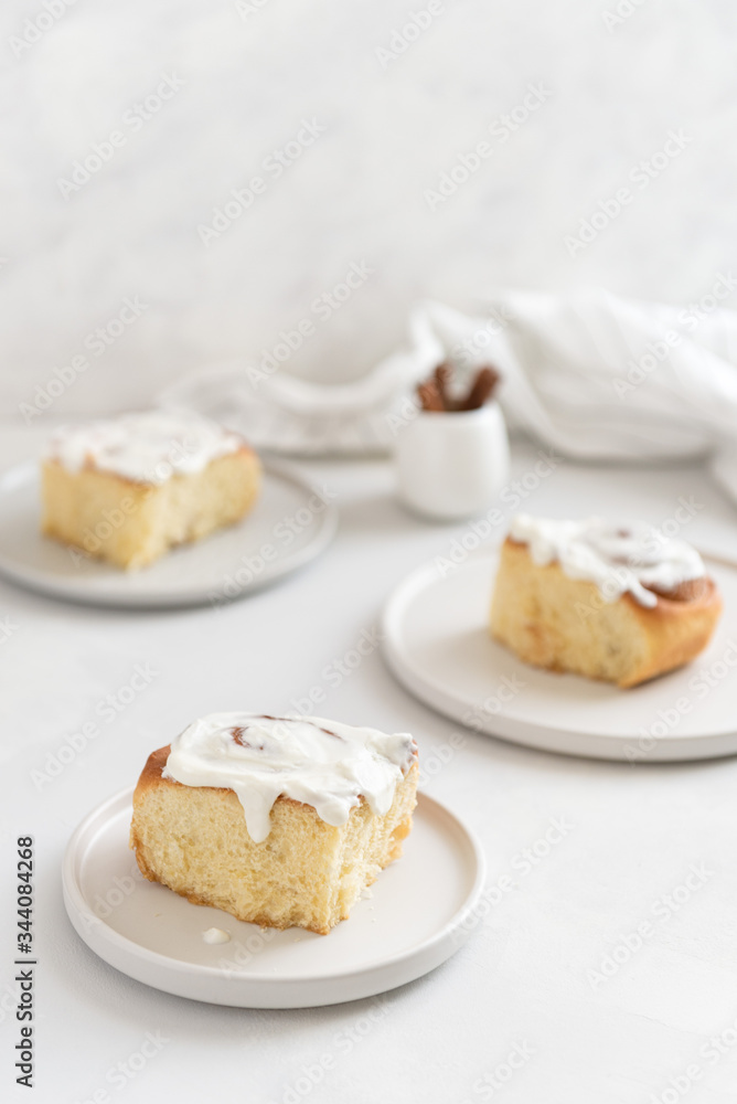 Fragrant freshly baked Cinnamon rolls or cinnabons covered with white cream glaze on the plates on white background. Cinnabons recipe. Traditional homemade sweet buns. Pastry, bakery. Copy space Fragrant freshly baked Cinnamon rolls or cinnabons covered with white cream glaze on the plates on white background. Cinnabons recipe. Traditional homemade sweet buns. Pastry, bakery. Copy space