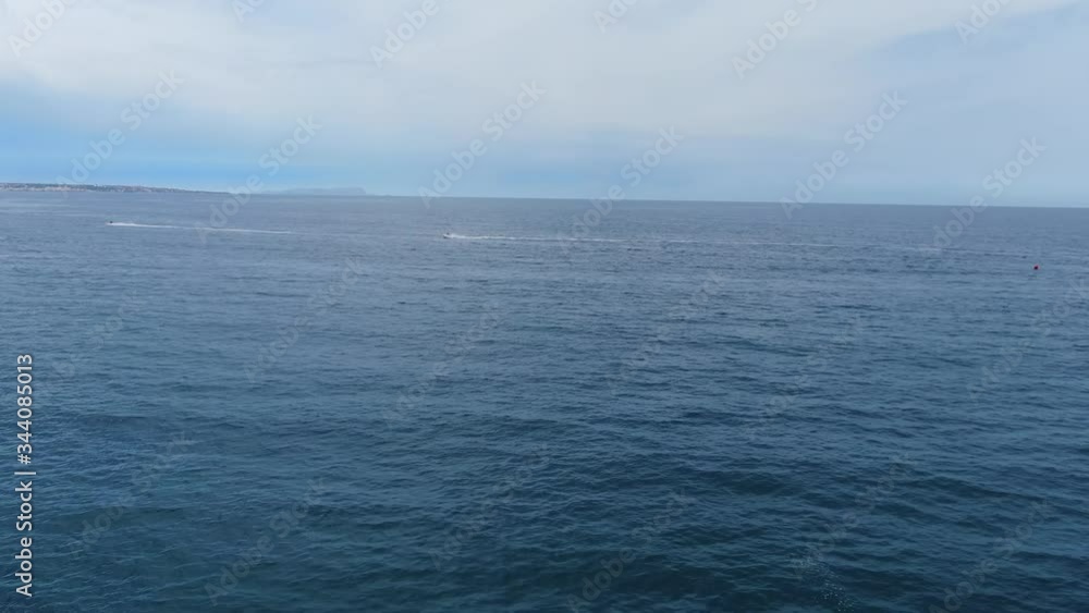 High aerial view of water skiers in distance in blue ocean water, one drives in foreground High aerial view of water skiers in distance in blue ocean water, one drives in foreground