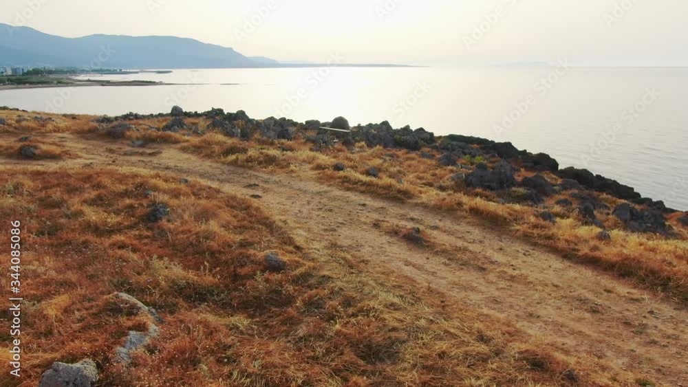 Aerial drone above grass and dirt road towards rocky cliffside and ocean, Greece Aerial drone above grass and dirt road towards rocky cliffside and ocean, Greece