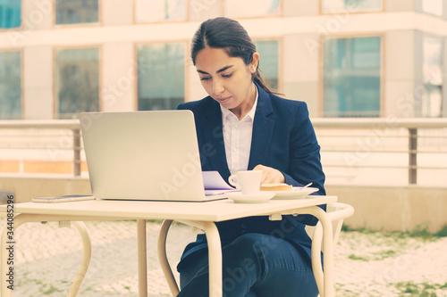 Businesswoman with laptop and papers in cafe. Foused young businesswoman working with papers and laptop computer while sitting in outdoor cafe. Business concept photo