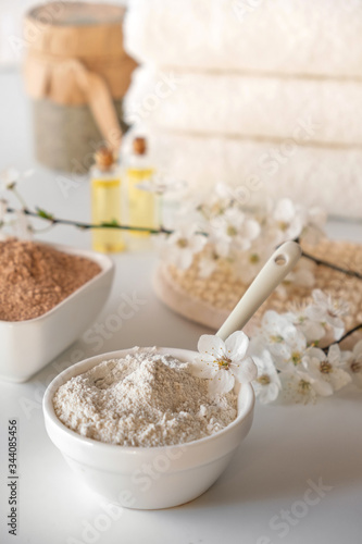 Ceramic bowl with white clay powder on white background. Ingredients for homemade facial and body mask or scrub and fresh sprig of flowering cherry . Spa and bodycare concept.