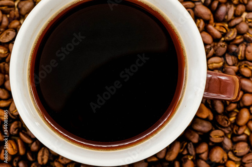 Coffee cup on wooden kitchen table with coffee beans. Top view with morning sunlight