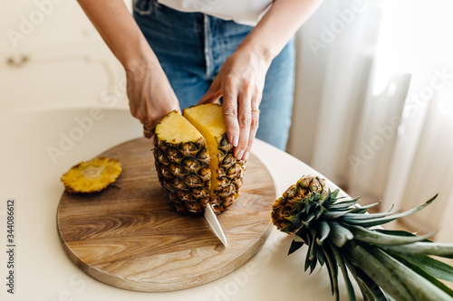 Woman cutting a fresh pineapple on a wooden board.