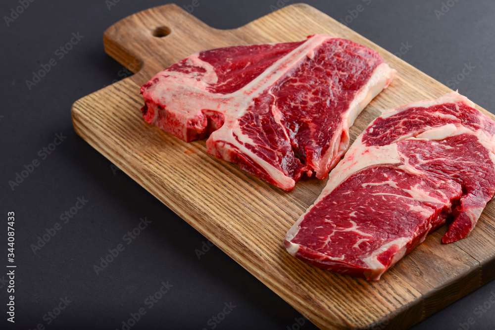 Fresh raw beef T-bone steak on wooden cutting board, top view. Porterhouse steak served over black background. Fresh raw beef T-bone steak on wooden cutting board, top view. Porterhouse steak served over black background.
