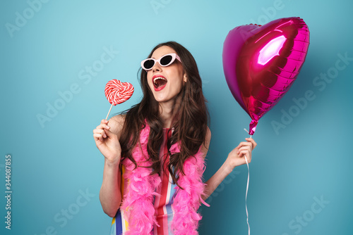 Photo of delighted young woman posing with balloon and lollipop