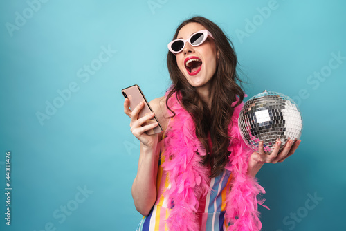 Photo of joyful young woman using smartphone and holding disco ball