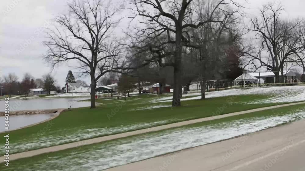 POV driving past rural municipal park with pond, playground equipment and picnic shelter in early spring POV driving past rural municipal park with pond, playground equipment and picnic shelter in early spring