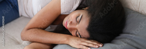 Portrait of young african-american woman sweetly sleeping on sofas pillow. Lovely female relaxing on couch and smiling while having nap. Relaxation and cozy concept