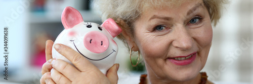 Cuadro en lienzo Portrait of cheerful aged grandmother with pink piggy bank