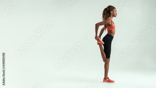 Staying flexible. Full length of young african woman with perfect body stretching her leg while standing against grey background