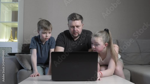 Focused cute boy and girl and their dad using laptop study online in app typing on computer exam sit at home sofa during the COVID 19 pandemic.