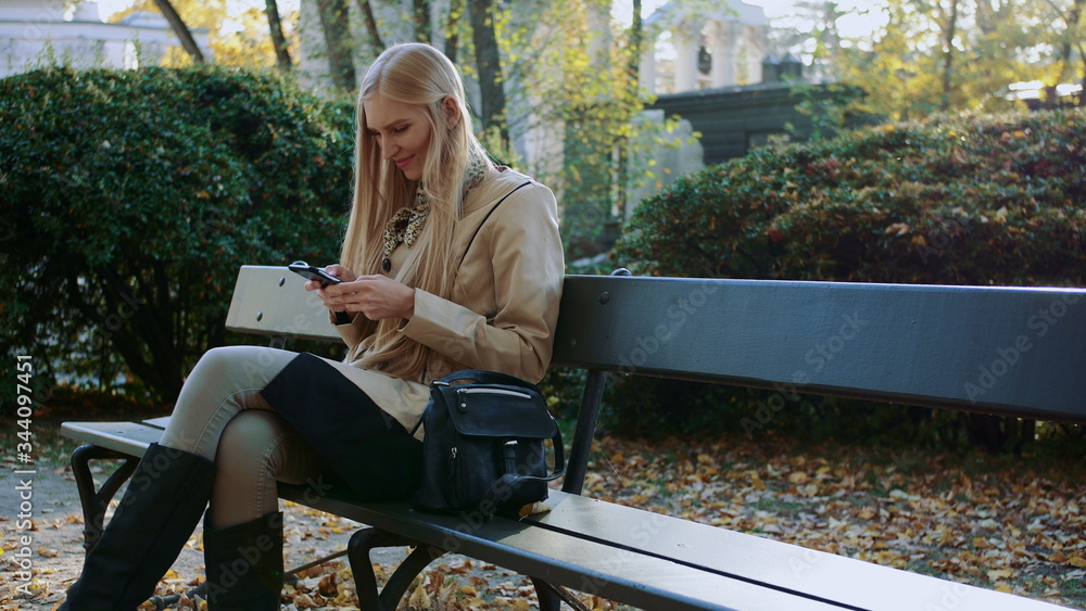 Fototapeta premium Girl communicates in a smartphone in a city park on a bench.