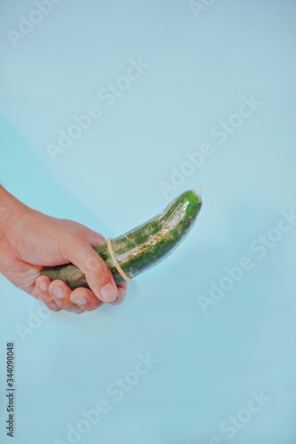Hand firmly gripping cucumber with condom with bright colorful background. 
