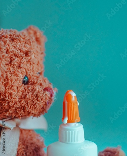 A teddy bear sniffs glue dripping from the nose of its container.