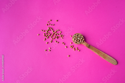 Wooden spoon of roasted buckwheat on buckwheat groat jar background, gluten free ancient grain for healthy diet, selective focus. Coronavirus food supplies. on a pink magenta background. top view. photo