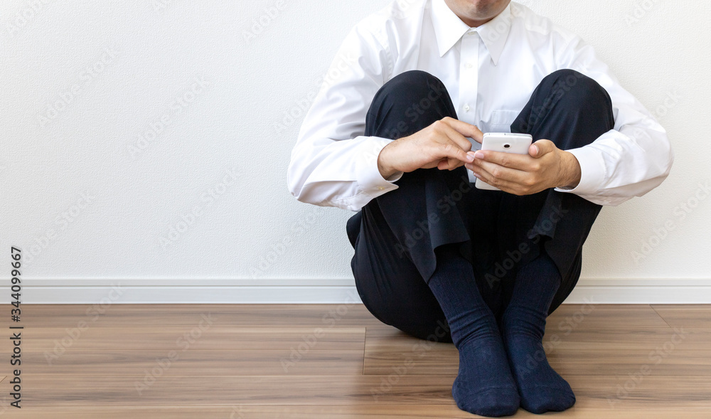 床に座ってスマートフォンを操作しているワイシャツを着た男性 床に座ってスマートフォンを操作しているワイシャツを着た男性