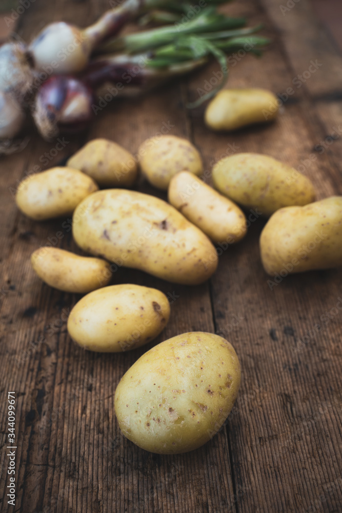 New potatoes, characteristic for their thin skin, are harvested when the ripening is not complete. In the photo typical Italian agricultural products potatoes and onions on wooden table New potatoes, characteristic for their thin skin, are harvested when the ripening is not complete. In the photo typical Italian agricultural products potatoes and onions on wooden table