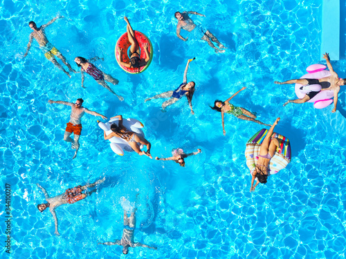 Aerial of friends having party in swimming pool with inflatable flamingo, swan, mattress. Happy young people relax at luxury resort on sunny day. View from above. Girls in bikini sunbathing in a sun. photo