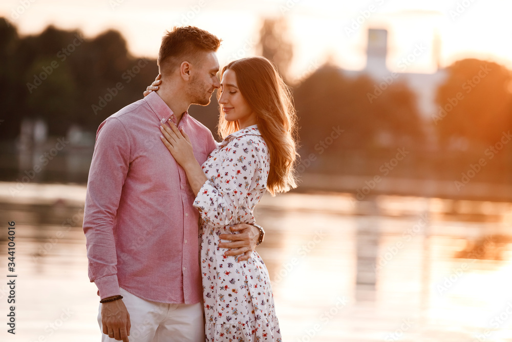 beautiful couple in love are standing and hugging near the lake on sunset. Lovely happy couple having fun near outdoors. happy holiday concept beautiful couple in love are standing and hugging near the lake on sunset. Lovely happy couple having fun near outdoors. happy holiday concept