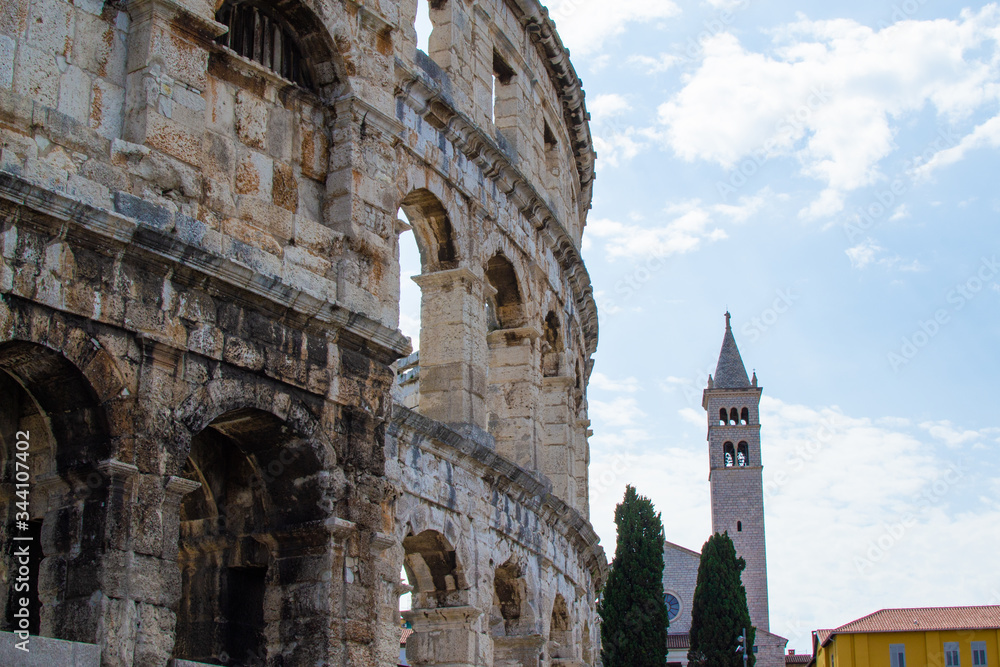 Wall of the Pula Arena, the only remaining Roman amphitheatre entirely preserved, with the tower of the Church of St Anthony at the background, in Pula, Croatia