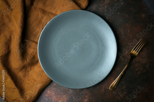 Empty plate on a dark background. Empty gray ceramic plate with a knife and fork for food and dinner on a dark beautiful background.