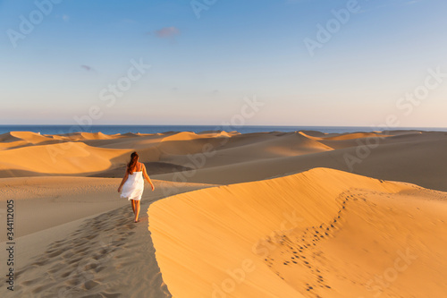 Young beautiful woman walking on the sand wearing white dress at maspalomas dunes bech. Gran Canaria, Spain photo