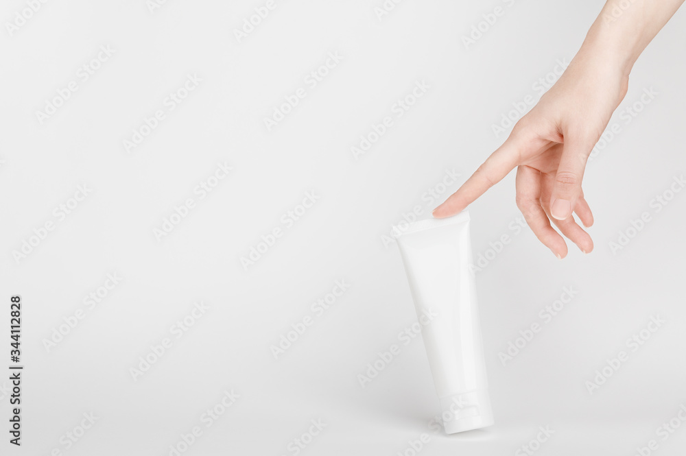 Female hand touching flacon for cream. Container for body lotion, toiletry. Tube for professional care products. Skincare and advertising concept. Mockup style and copy space. Isolated on gray