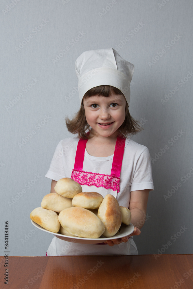Little girl in a cook suit holds a plate with fresh pastries Little girl in a cook suit holds a plate with fresh pastries