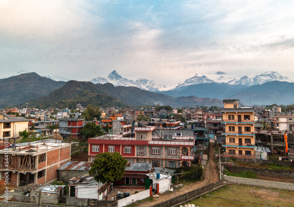 Obraz premium A view of the snow capped Annapurna range over the rooftops of the concrete houses of the city of Pokhara in Nepal.