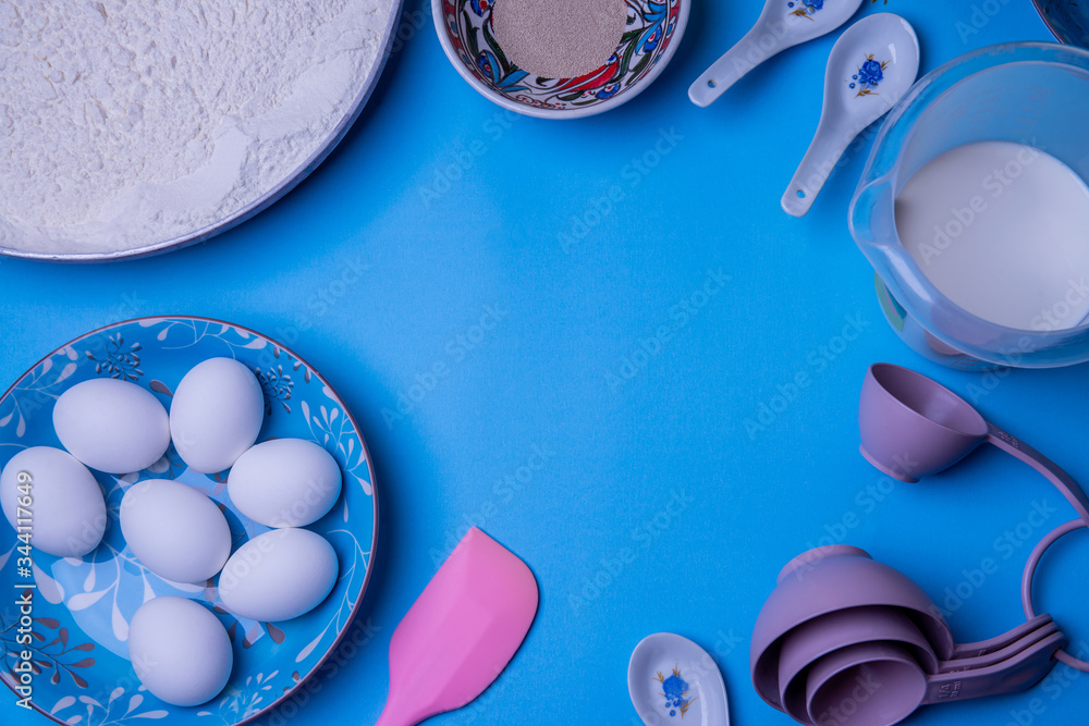 Ingredients and tools for baking - flour, eggs measure cups on blue background. Lay flat. Top view. Copy space Ingredients and tools for baking - flour, eggs measure cups on blue background. Lay flat. Top view. Copy space