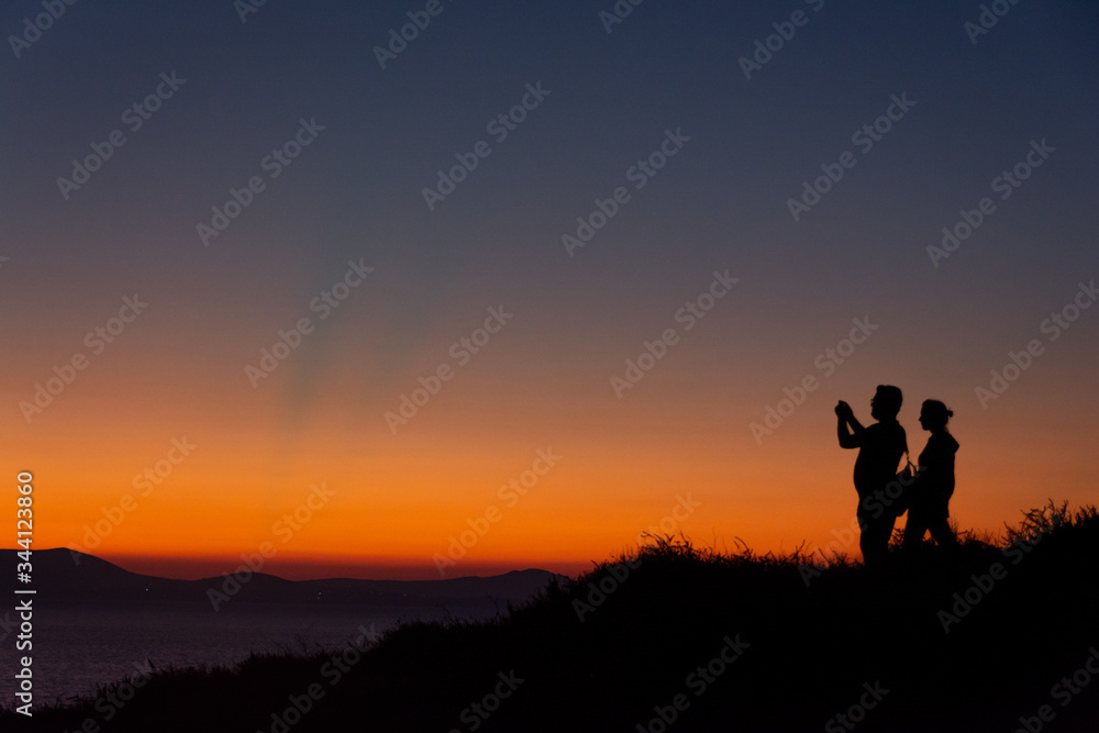 Silhouette of couple standing on mountain taking photo at sunset