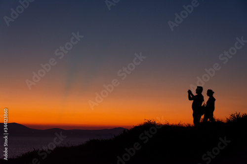 Silhouette of couple standing on mountain taking photo at sunset