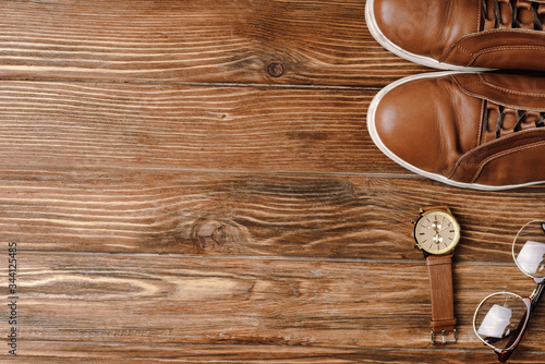 Top view of mens brown casual shoes, wristwatch and glasses on wooden background