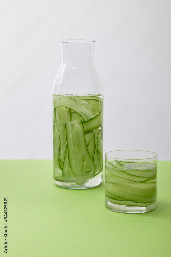 Bottle and glass with drink made of sliced cucumbers isolated on grey Bottle and glass with drink made of sliced cucumbers isolated on grey