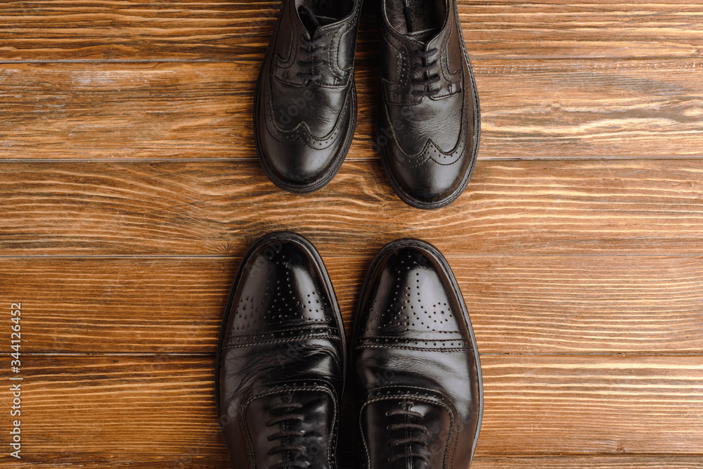 Top view of mens and childrens black elegant shoes on wooden background, fathers day concept Top view of mens and childrens black elegant shoes on wooden background, fathers day concept