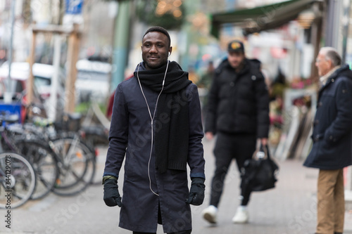 Young Black Man with Earphones Standing on Sidewalk