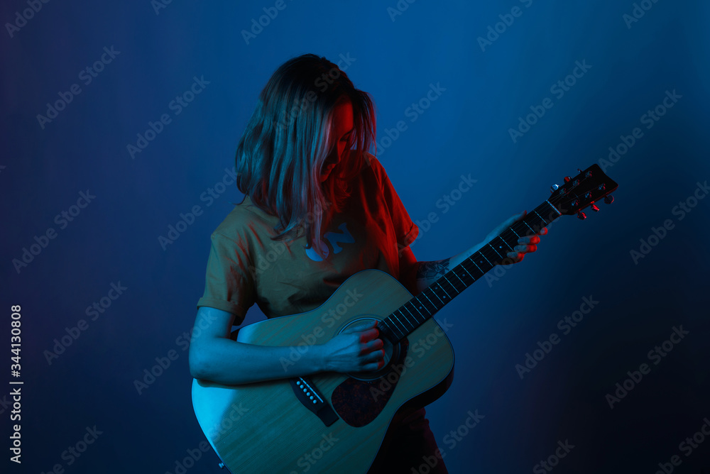 Short hair girl is enjoying and playing her guitar in blue and red light.