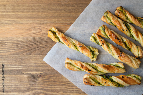salty sticks of puff pastry sprinkled with cumin and greenery on a wooden background