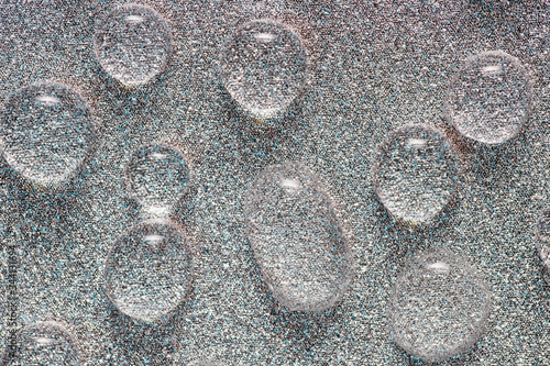 Abstraction with large drops of a transparent liquid on a silver mother-of-pearl surface, photographed close-up.