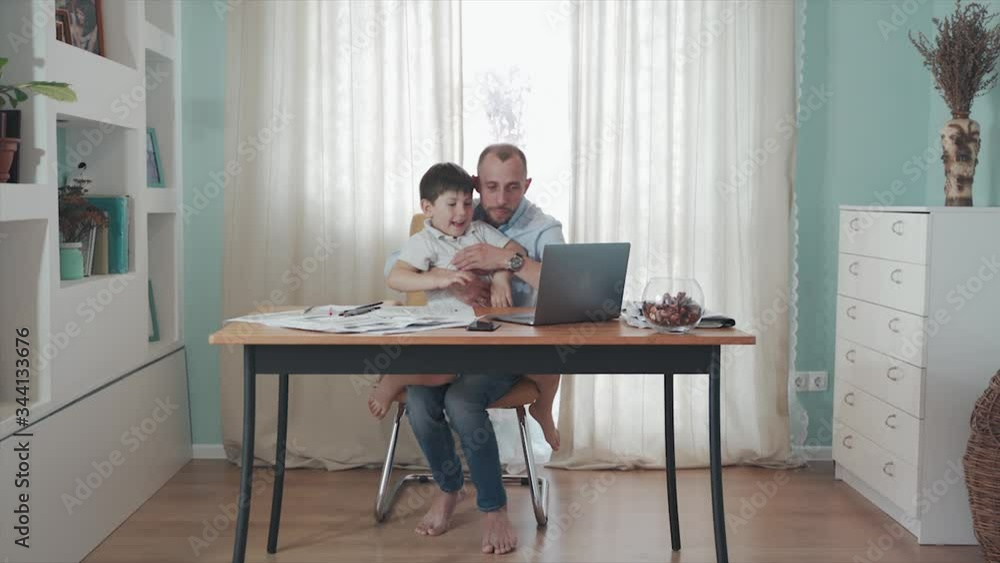 Parent working online from home. Remote work. Family on self-isolation. Home office. Dad and son enjoy their time together playing computer. Happy childhood. Paternity. Quarantine. Epidemic. Crisis. Parent working online from home. Remote work. Family on self-isolation. Home office. Dad and son enjoy their time together playing computer. Happy childhood. Paternity. Quarantine. Epidemic. Crisis.