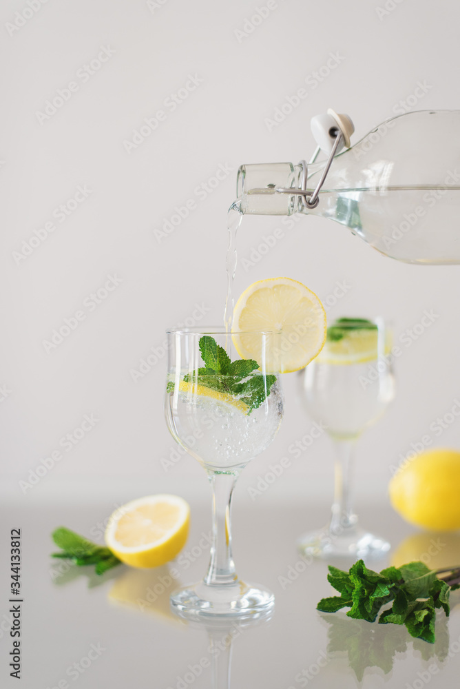 Sparkling mineral water with sliced lemon and fresh mint leaves. Pouring water into a glass. Citrus lemonade