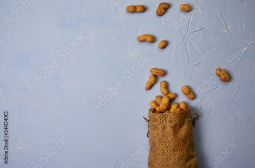 peanuts dropped from a linen bag on a blue textural background top view, place for text, copy space © Денис Родионов