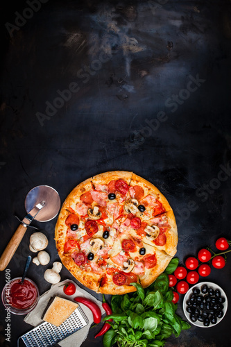 Traditional Italian pizza on a dark table with ingredients. Pizza menu. Space for text.