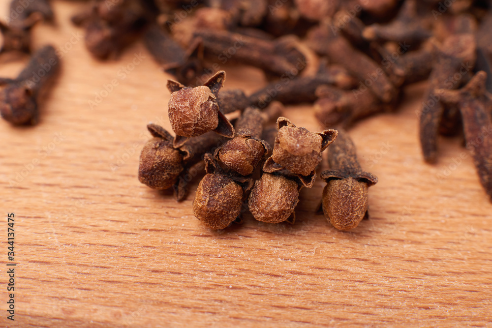 A spice of dried cloves lies on a wooden spoon and is scattered on old wooden boards near the bag. Spices cloves for cooking. Close-up. A spice of dried cloves lies on a wooden spoon and is scattered on old wooden boards near the bag. Spices cloves for cooking. Close-up.