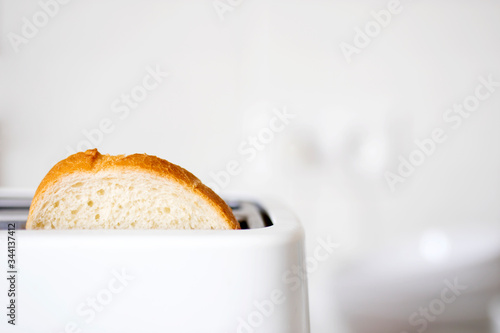 A piece of bread in a toaster on the background of a white ceramic blurred kitchen wall