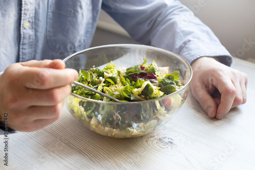 A man in a blue office shirt is sitting at a table with a bowl of salad. Cherry tomato salad with rucola, radicchio, lettuce, feta cheese, olive oil and balsamic dressing