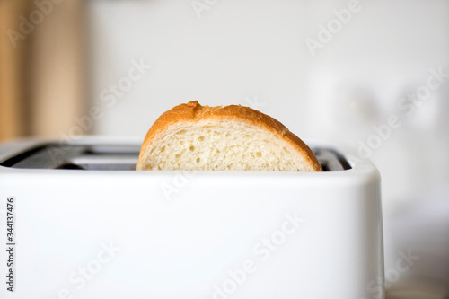 A piece of bread in a toaster on the background of a white ceramic blurred kitchen wall