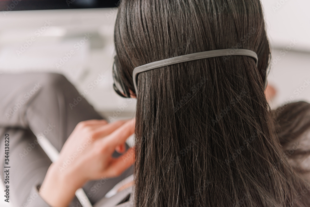 Fototapeta premium back view of brunette remote operator in headset working at home