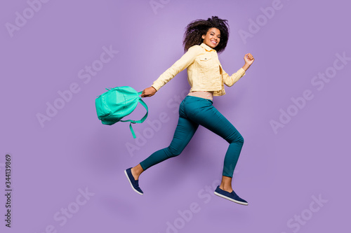 Full length body size profile side photo of cheerful toothy positive girl in pants trousers yellow jacket footweat running jumping isolated pastel color background violet holding satchel photo