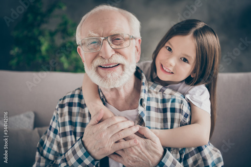 Closeup photo of funny two people old grandpa little granddaughter sitting sofa stay home quarantine safety hugging piggyback modern design interior living room indoors photo